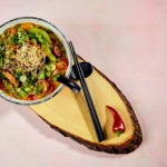Zdjęcie jedzenia przedstawiające miskę zupy Tom Yum and drewnianej podkładce. fotografia kulinarna